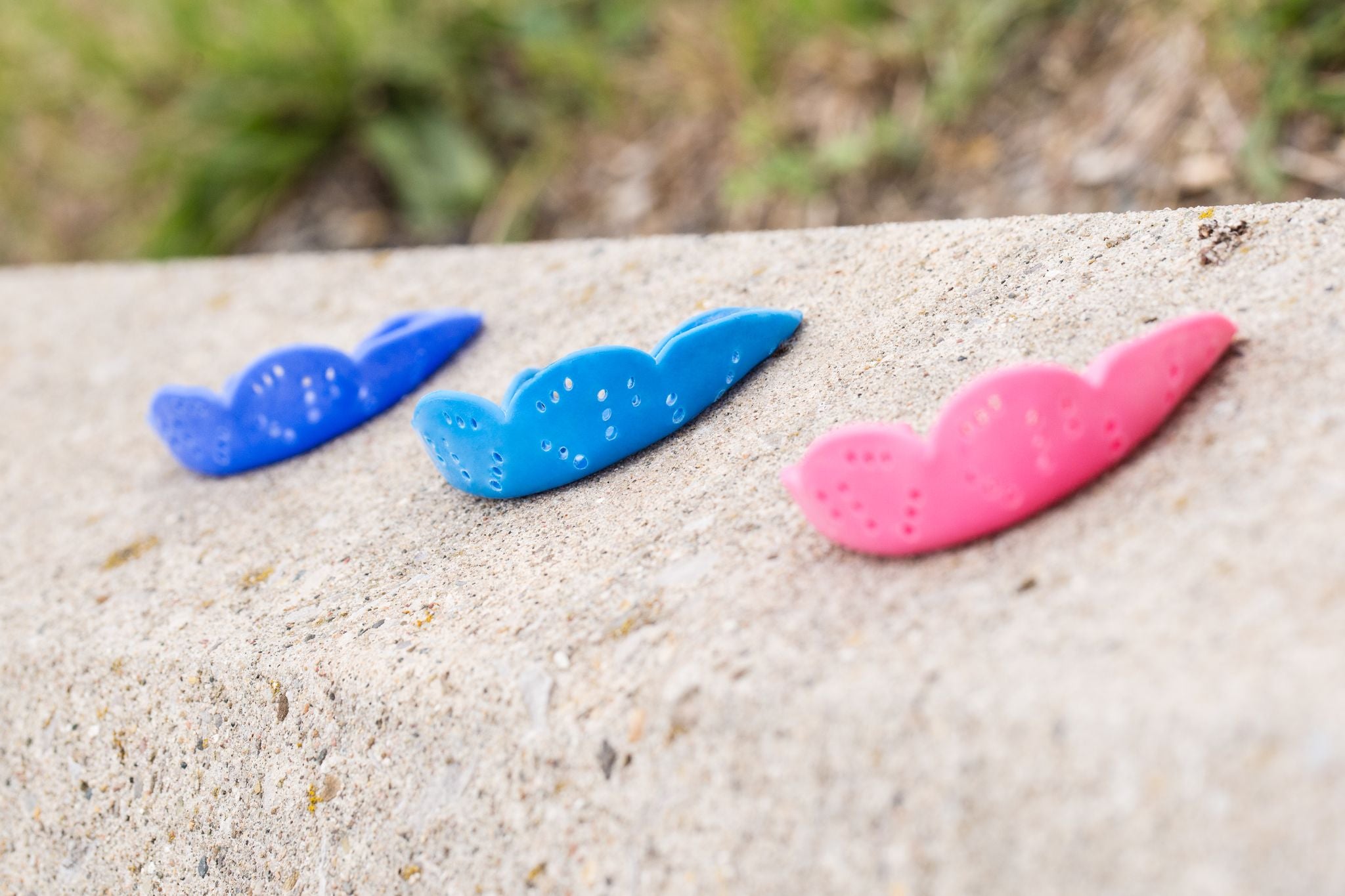 Mouthguards of different colours lined up on a concrete wall.